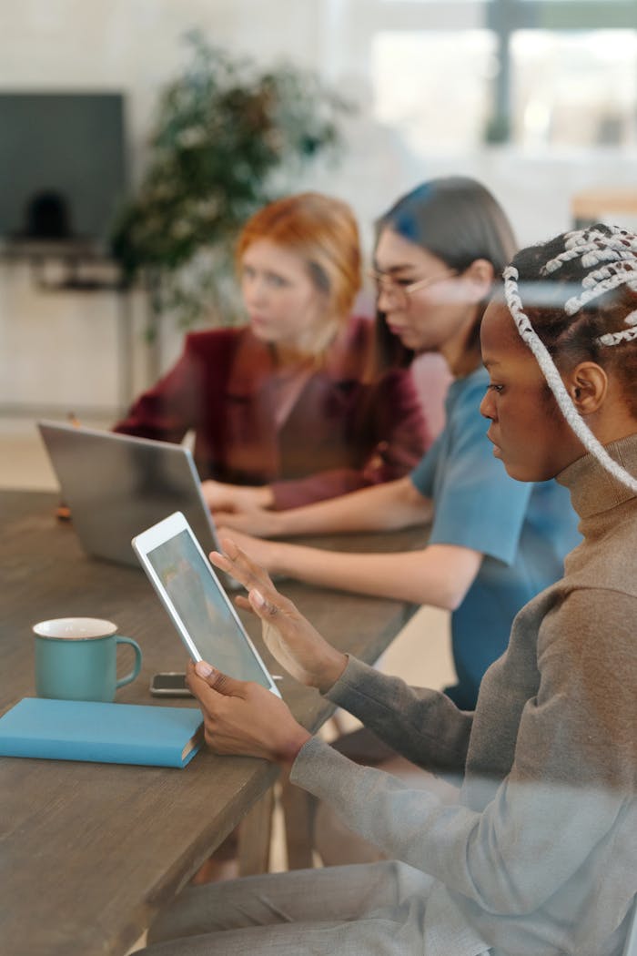 Multicultural group of women working on digital devices in a contemporary office setting.